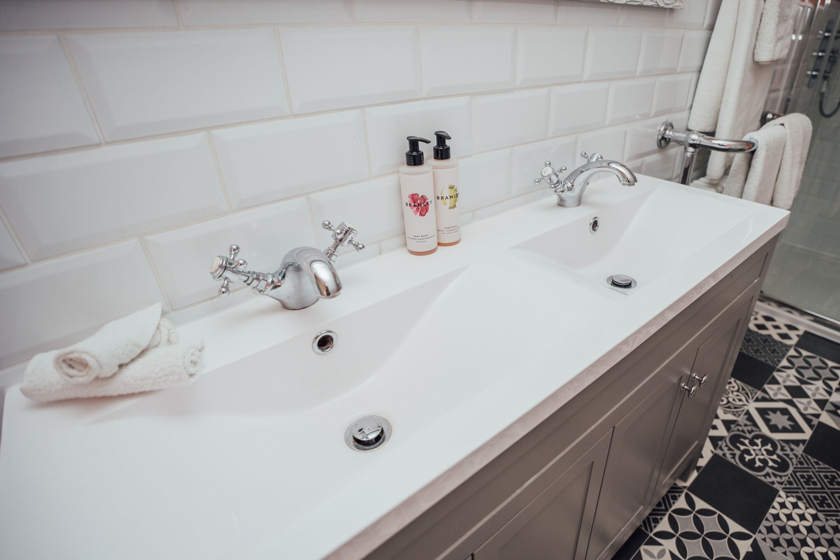 A bathroom with a double sink, two faucets, and two bottles of shampoo.