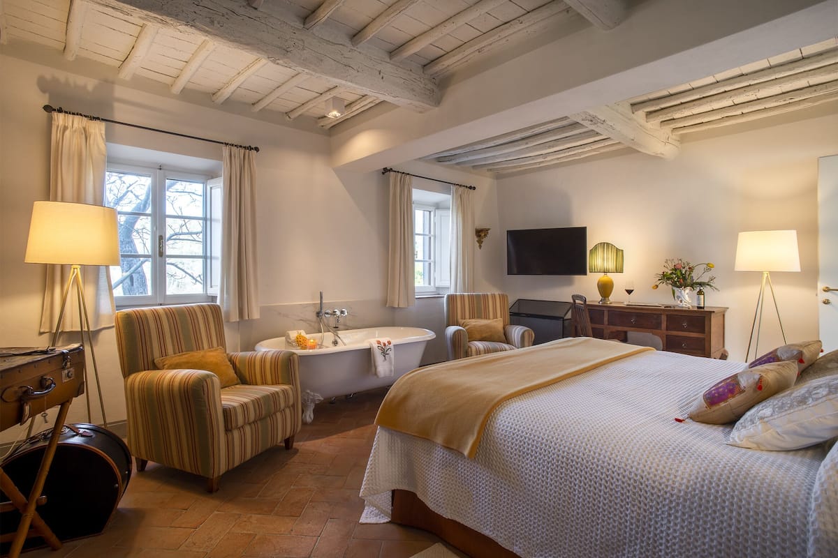 Habitación de hotel con una cama grande, un área de descanso con una silla, un escritorio, una bañera y un televisor en la pared.