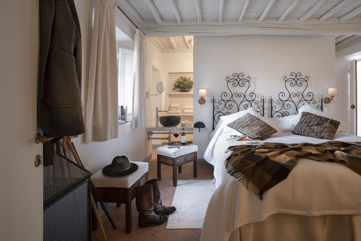 Un dormitorio con una cama, una mesita de noche y una silla. Se observa un perchero con un abrigo colgado.