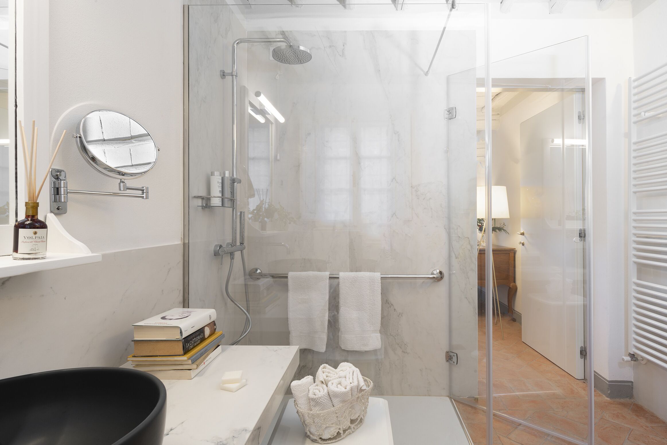Un baño moderno con cabina de ducha de vidrio, encimera de mármol, espejo redondo y toallero.