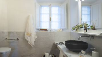 Un baño con pared de mármol, un lavabo tipo cuenco negro, un inodoro blanco, un perchero y una ventana con vistas al exterior.