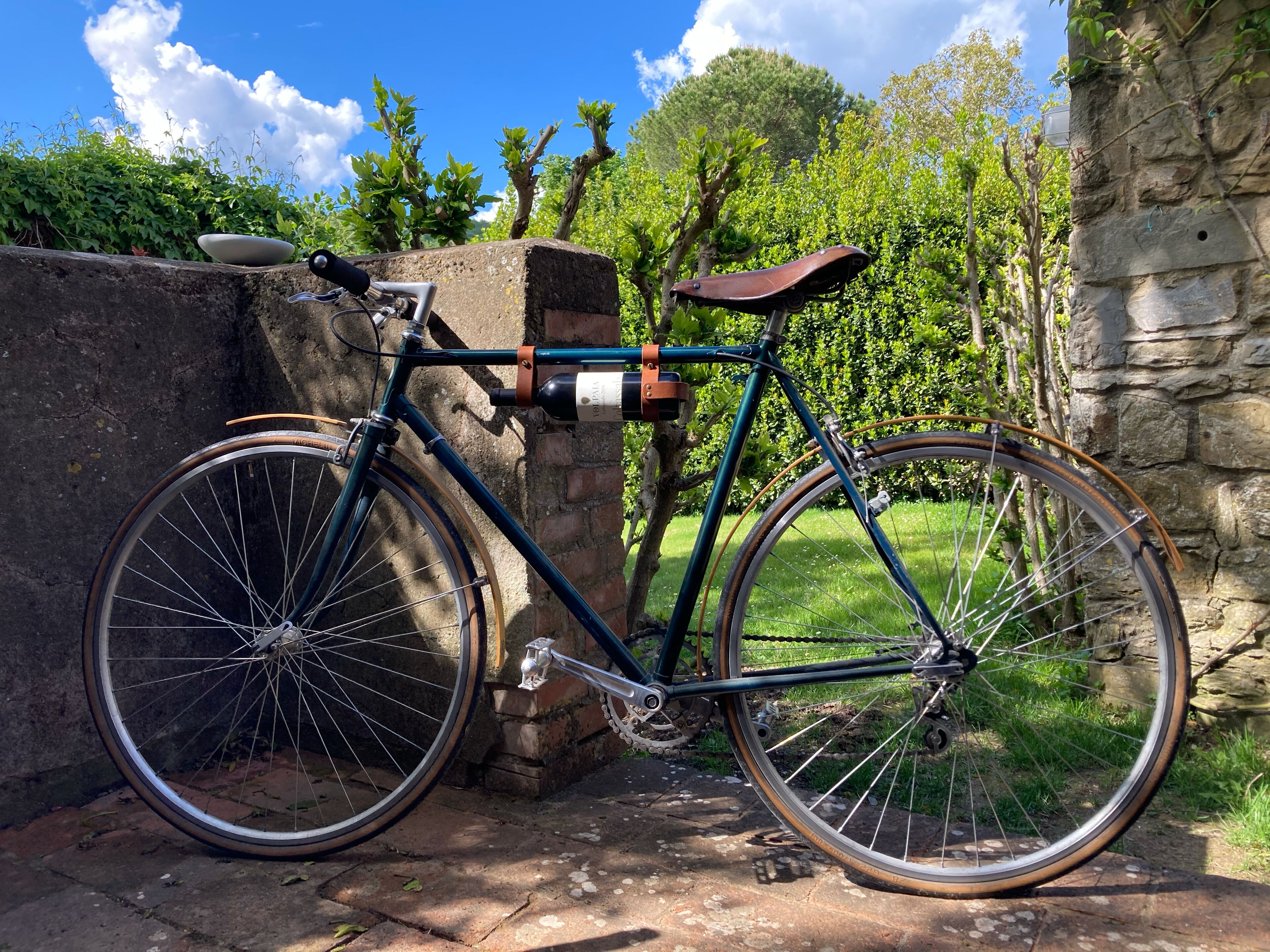 Un vélo ancien est garé contre un mur de pierre, dans un jardin.