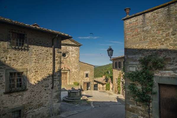 A narrow street with stone buildings, a central fountain, and a clear blue sky.