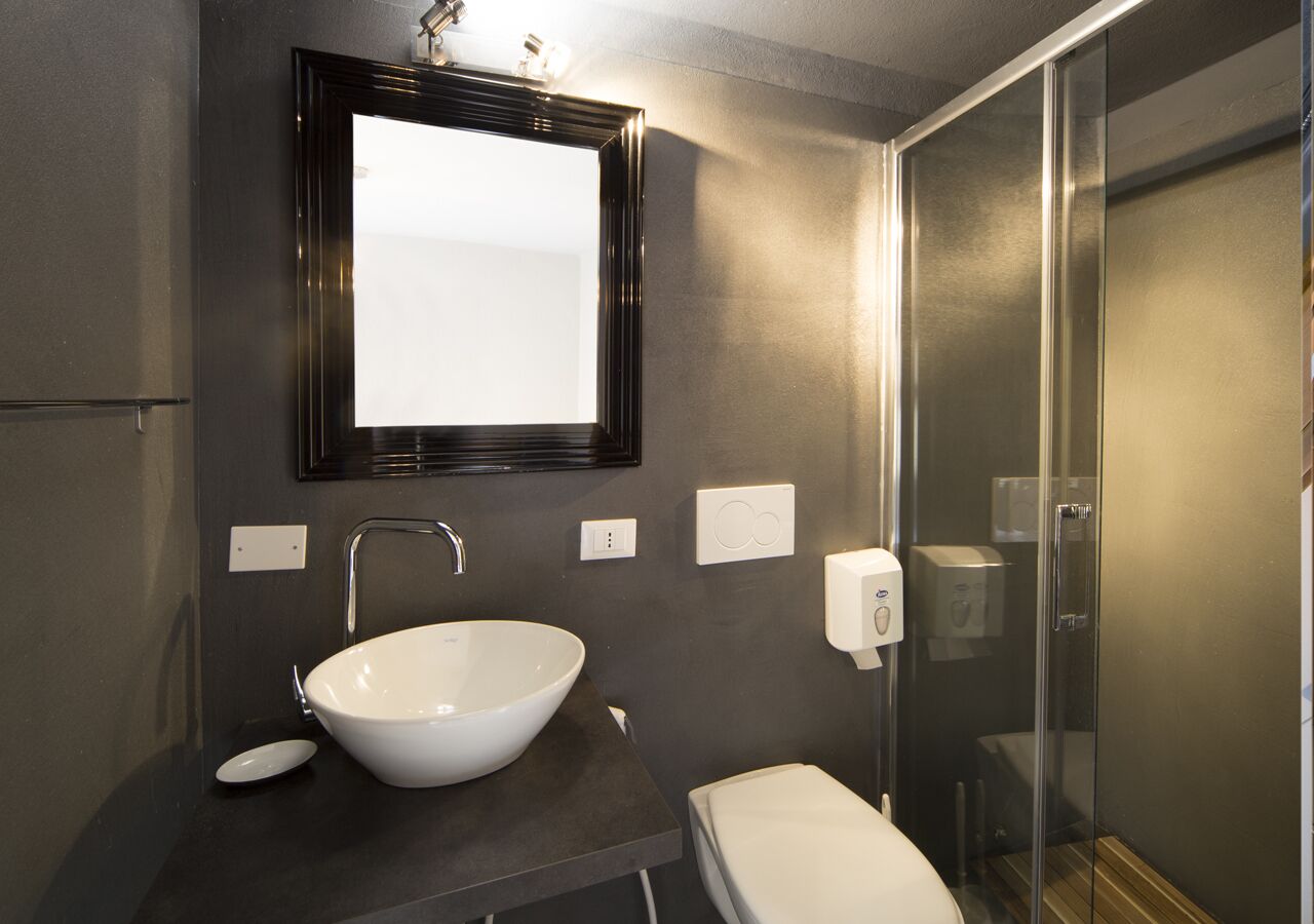 Un baño moderno con un lavabo blanco de diseño, un espejo, un inodoro y una cabina de ducha con paredes de vidrio.