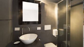 Un baño moderno con un lavabo blanco de diseño, un espejo, un inodoro y una cabina de ducha con paredes de vidrio.