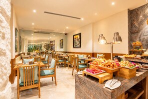 Un comedor de hotel con mesas y sillas de madera, un bufé con diferentes opciones de comida y una pared de mármol con un cuadro.