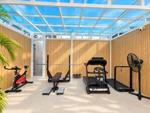 Une salle de sport équipée de matériel d’exercice, d’un tapis de course et d’un ventilateur.