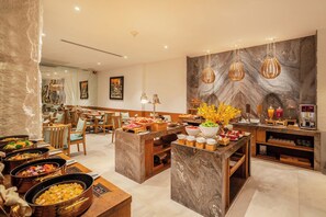 A hotel dining area with a marble wall, wooden furniture, and a buffet with various food options. - A&EM Art Hotel (Ho Chi Minh City)