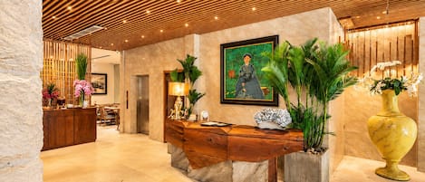 A reception area with a wooden reception desk, a marble floor, a large painting, and potted plants.