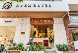 Exterior del hotel A&EM Art Hotel con fachada moderna, entrada visible y un cartel con la dirección.