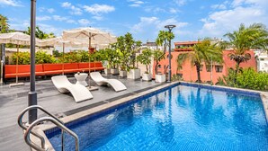 A swimming pool with lounge chairs and umbrellas, surrounded by greenery and buildings. - A&EM Art Hotel (Ho Chi Minh City)