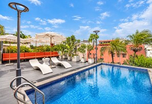 Ein Swimmingpool mit Liegestühlen und Sonnenschirmen, umgeben von Grünflächen und Gebäuden.