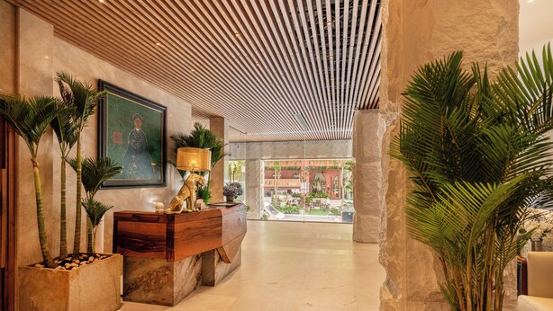 A lobby with a wooden reception desk, a framed portrait, and a large potted plant. - A&EM Art Hotel (Ho Chi Minh City)