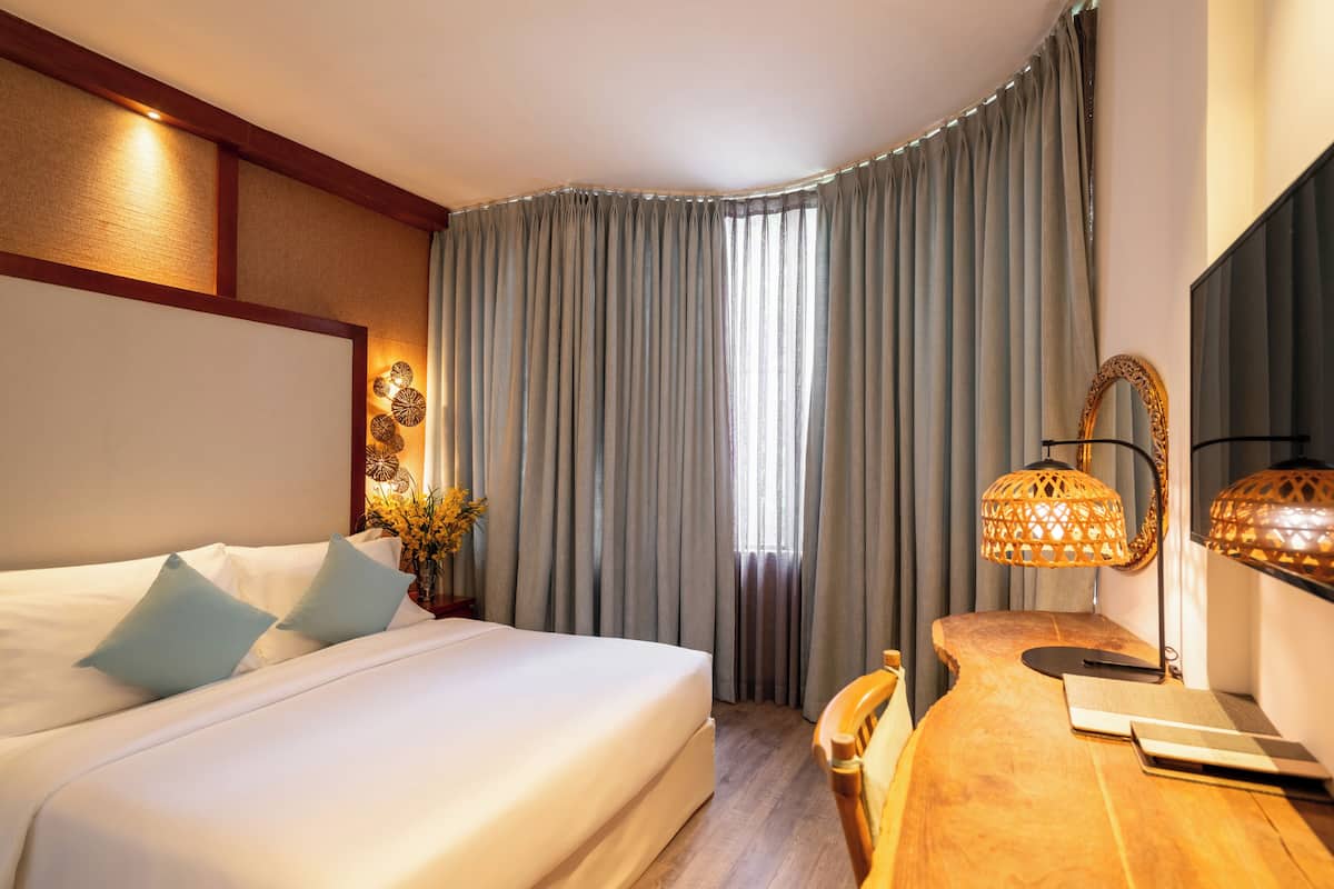 Une chambre d’hôtel avec un grand lit, un bureau en bois, un ordinateur portable et une télévision.