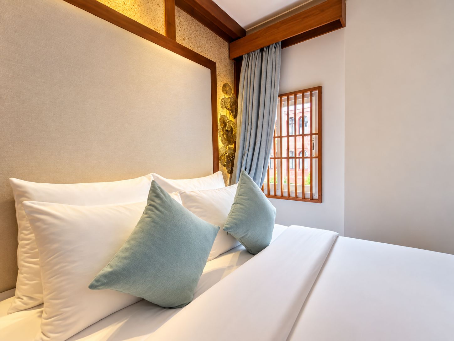 A hotel room with a bed, pillows, a window with bars, and a curtain.