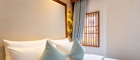 A hotel room with a bed, pillows, a window with bars, and a curtain.
