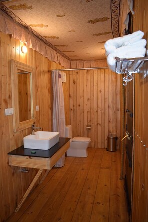 A wooden-paneled bathroom with a sink, toilet, and shower curtain. - Govardhan Eco Village (Vada)