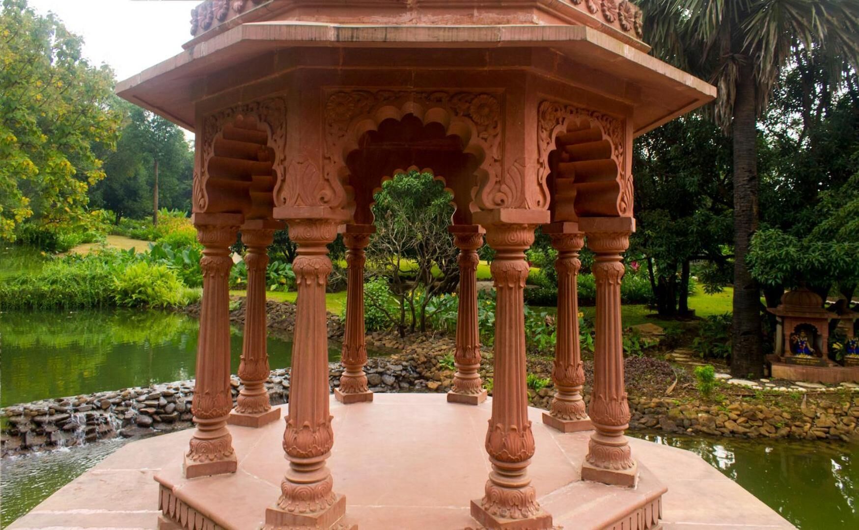 A pavilion with intricate carvings and a pond in the background.