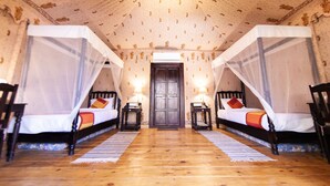 A room with two beds, each with a canopy, a wooden floor, and a door in the center. - Govardhan Eco Village (Vada)