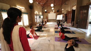 A yoga class in a room with brick walls, wooden beams, and a high ceiling. - Govardhan Eco Village (Vada)