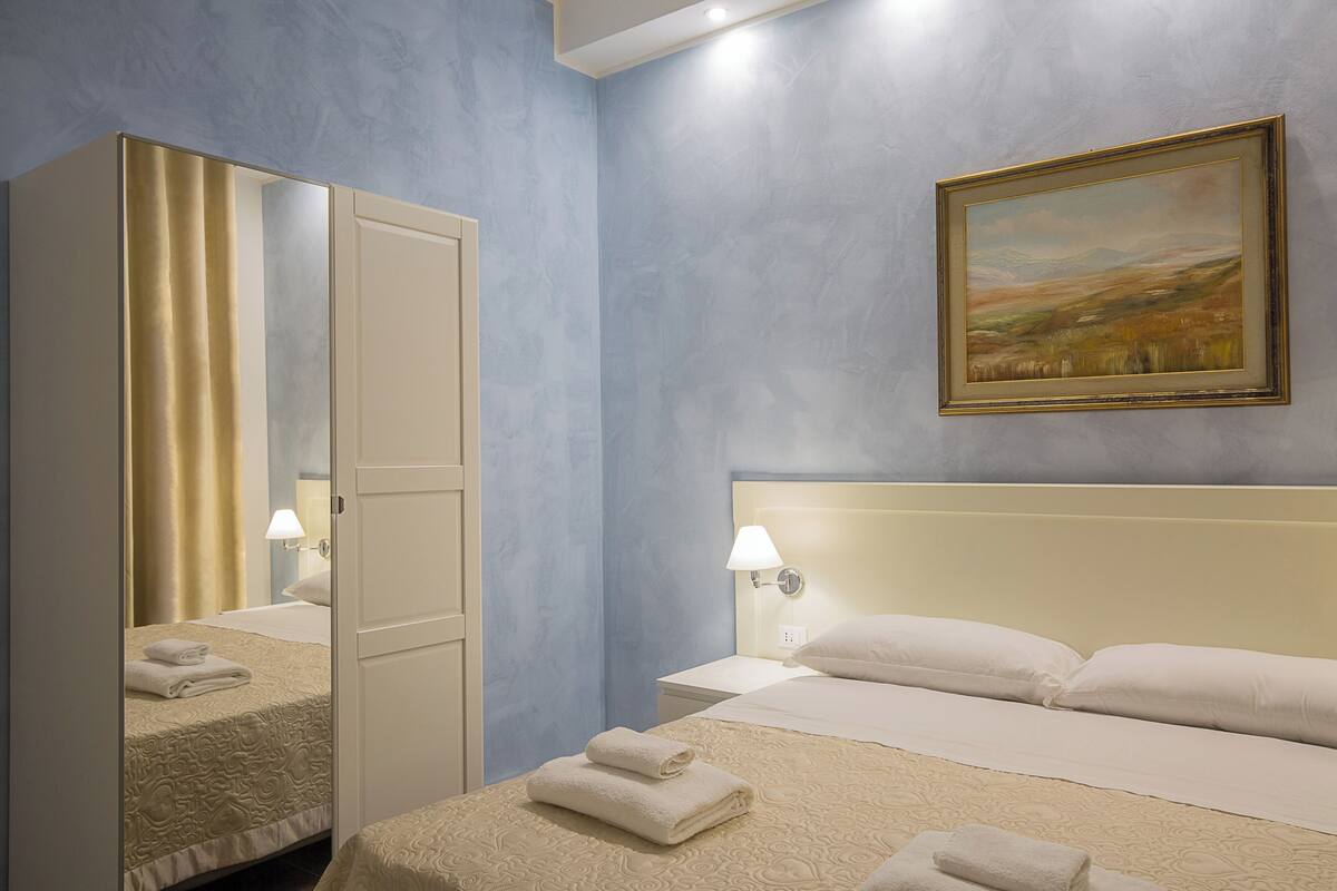 Ein Hotelzimmer mit Bett, Nachttisch, Lampe, einem Bild an der Wand und einem Schrank.