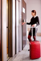 Una persona con una valigia rossa in piedi accanto alla porta di un ascensore.
