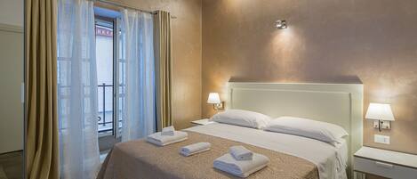Habitación de hotel con una cama grande, dos mesitas de noche y vistas al exterior a través de una ventana con cortinas.
