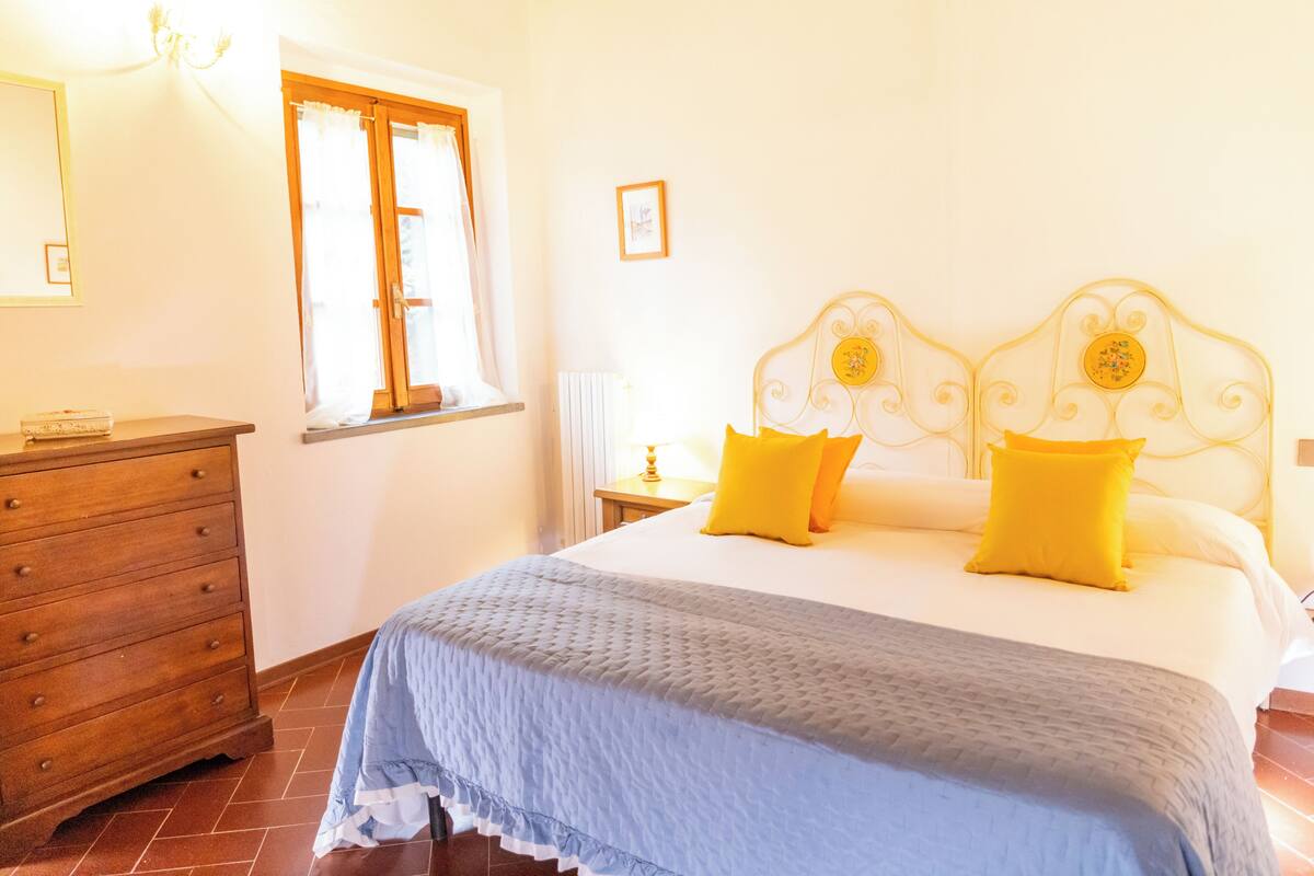 Une chambre à coucher avec un lit, une commode, une fenêtre avec des rideaux et un tableau accroché au mur.