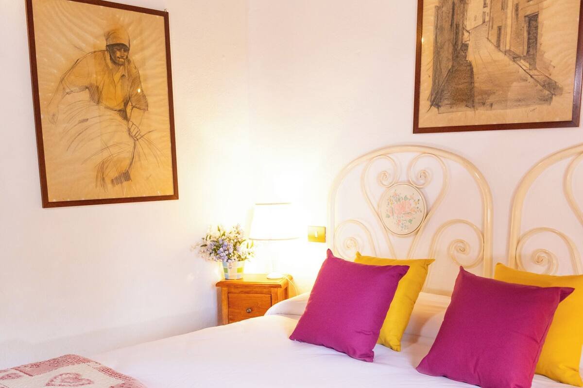 Un lit recouvert d’une couvre-lit à motifs, une table de chevet ornée d’un vase de fleurs et deux œuvres d’art encadrées accrochées au mur.