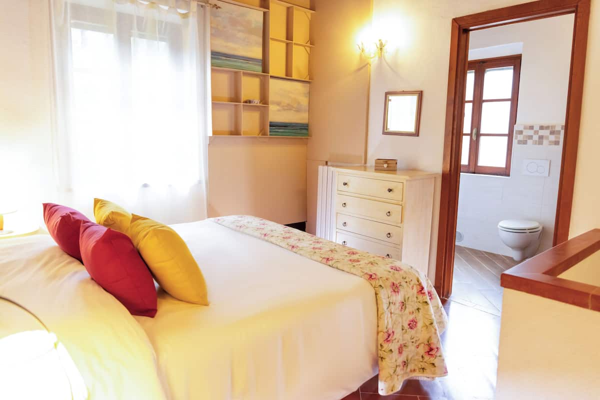 Une chambre à coucher avec un lit, une commode, un miroir et une salle de bain visible à travers une porte ouverte.