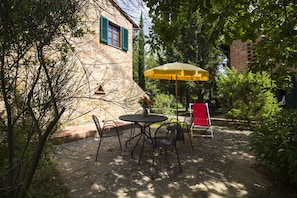 A stone building with a window and a yellow umbrella. There are chairs and a table in front of the building. - Borgo Il Poggio Agriturismo (Montaione)