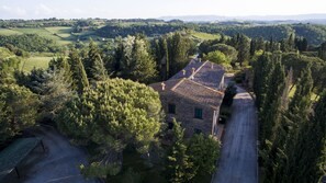 A stone house with a tiled roof surrounded by dense trees and rolling hills in the background. - Borgo Il Poggio Agriturismo (Montaione)