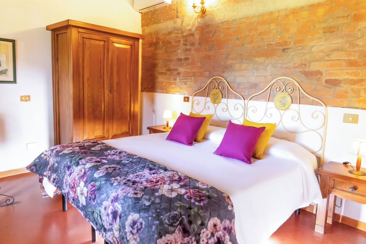Une chambre avec un grand lit, une armoire en bois, un mur en briques et une table de chevet avec une lampe.