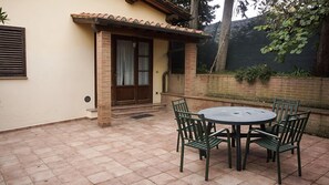 A patio with a round table and four chairs, a door with a window, and a brick wall. - Agriturismo Cameli (Certaldo)