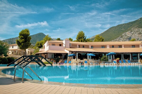 A swimming pool with lounge chairs and umbrellas, surrounded by buildings and mountains. - Club Esse Cala Gonone Beach Village (Dorgali)