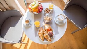 Ein Frühstückstisch mit Croissants, Obst, Keksen und Getränken in einem Raum mit modernen Stühlen.