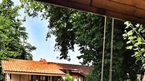 A rustic house with a tiled roof, surrounded by a garden with a gravel path, wooden stumps, and a hammock.