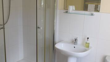 Baño con ducha de vidrio, lavamanos sobre pedestal, inodoro y espejo sobre el lavamanos.
