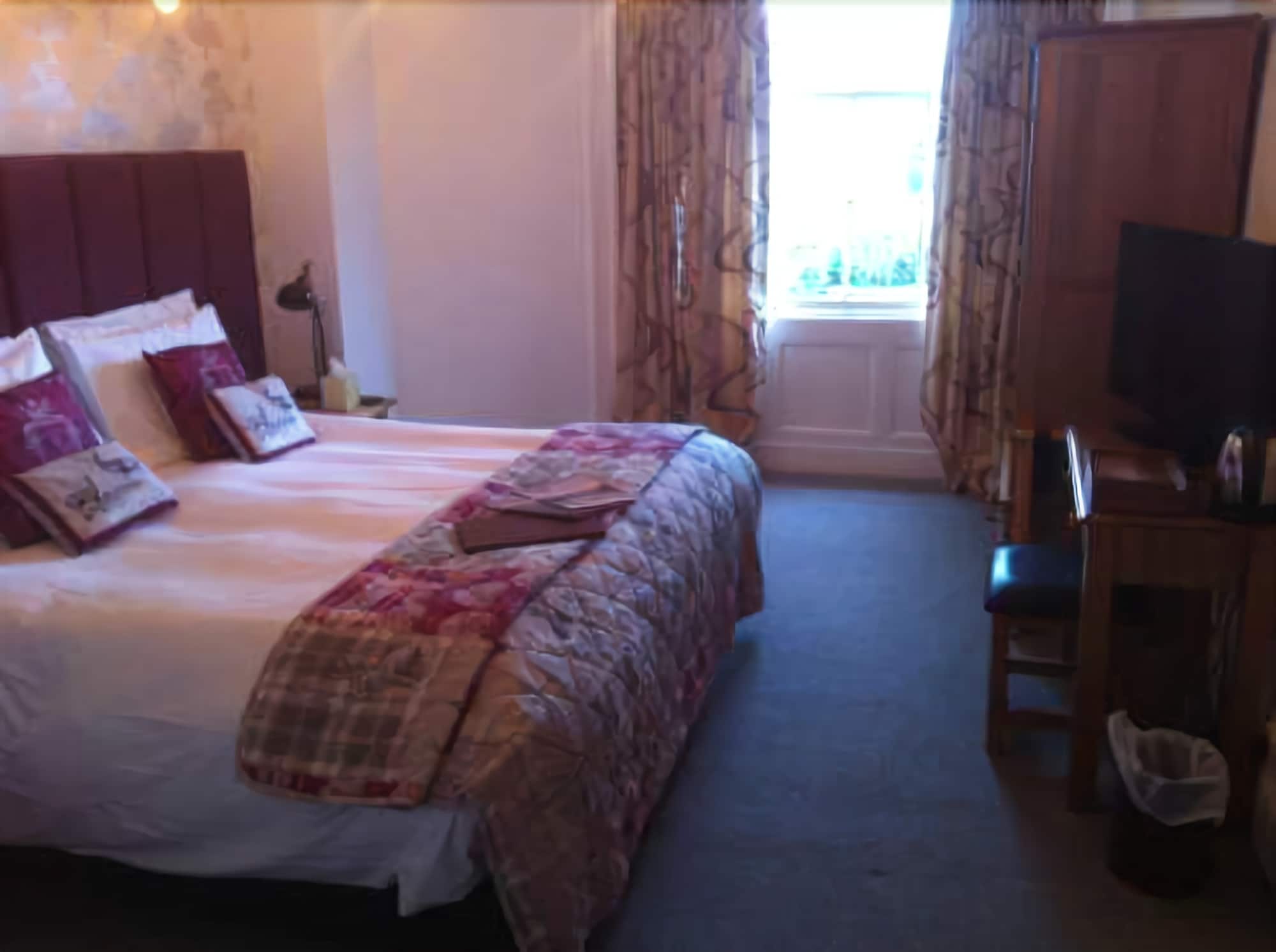 A hotel room with a bed, a desk, a television, and curtains.