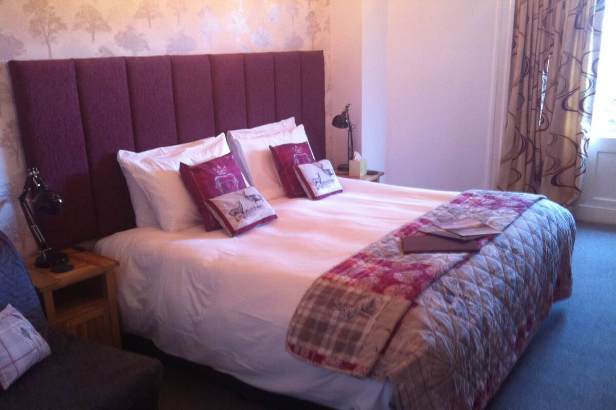 A neatly made bed with a headboard, two bedside tables with lamps, and a chair.