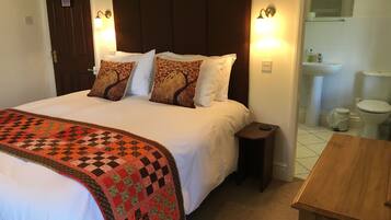 Habitación de hotel con una cama grande, una mesita de noche de madera, una pequeña mesa y un baño visible a través de una puerta abierta.