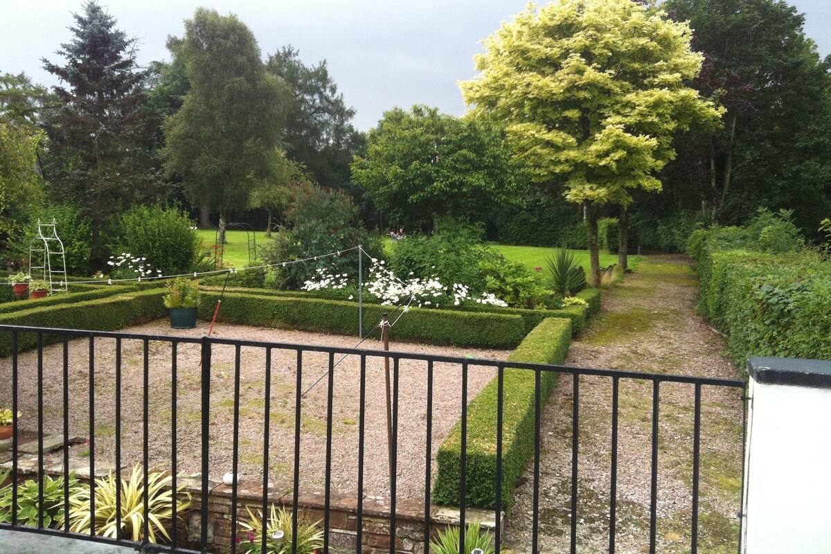 A well-maintained garden with neatly trimmed hedges, a variety of trees, and a gravel path.