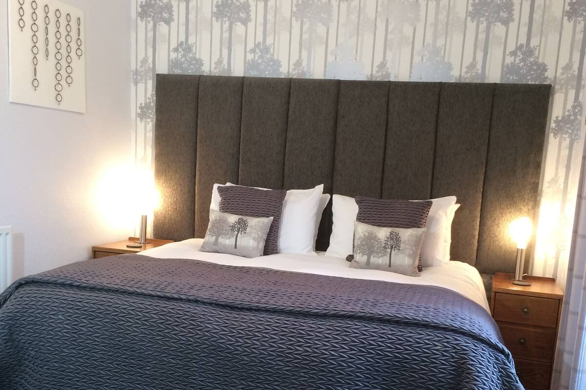 A neatly arranged bedroom with a large bed, two bedside tables, and a chair.