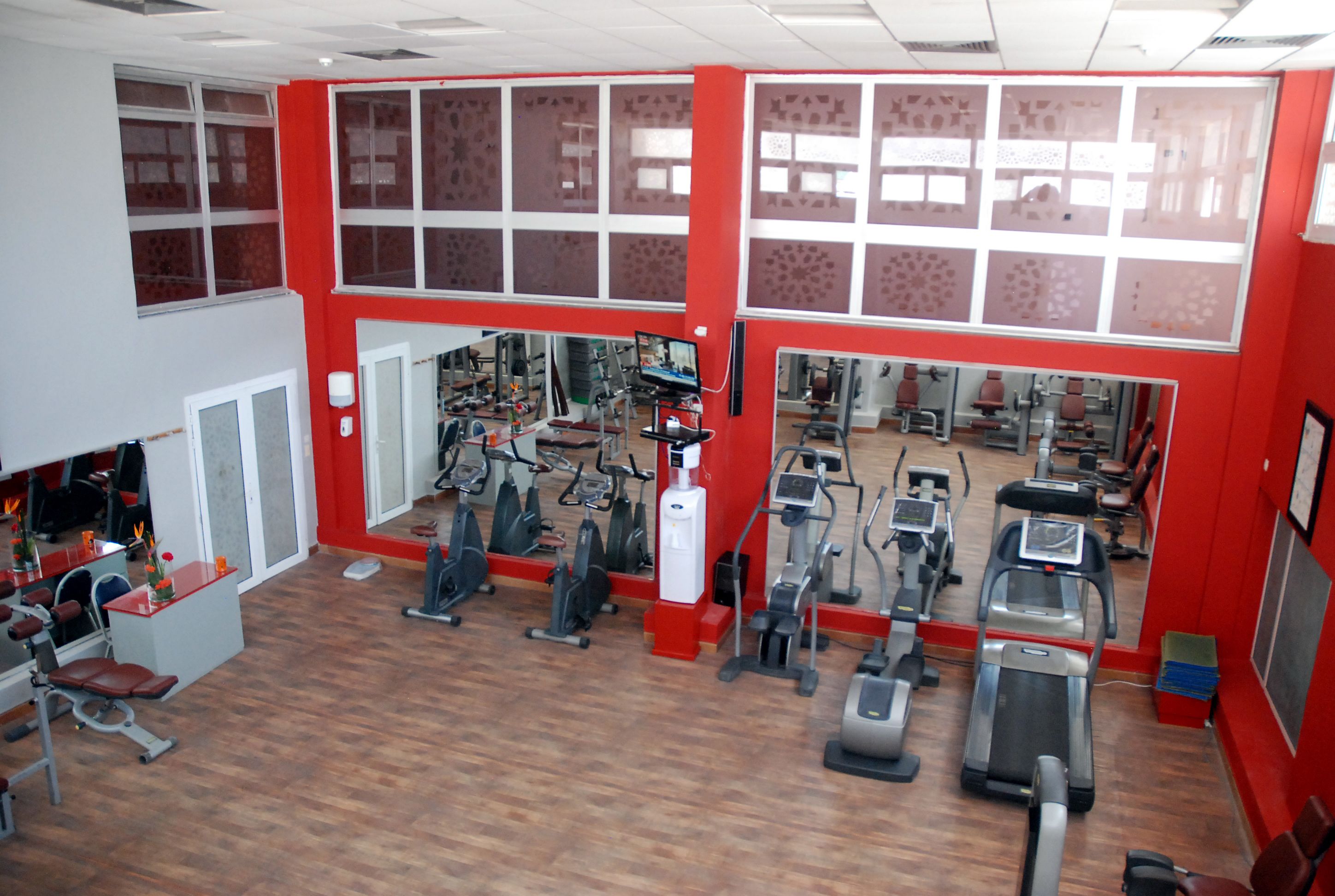 A gym with various exercise equipment, a reception desk, and a large mirror wall.