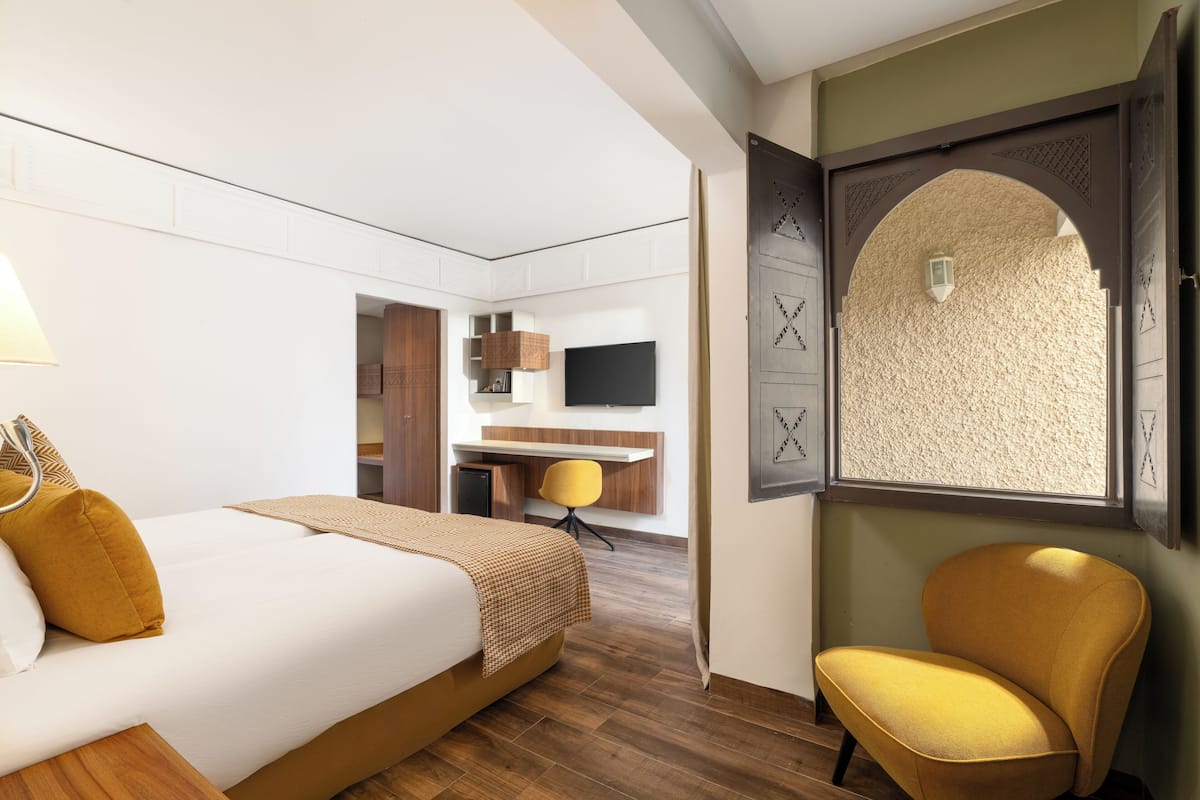 Ein Hotelzimmer mit einem Bett, einem Schreibtisch, einem Stuhl und einem Fenster mit strukturierter Wand.