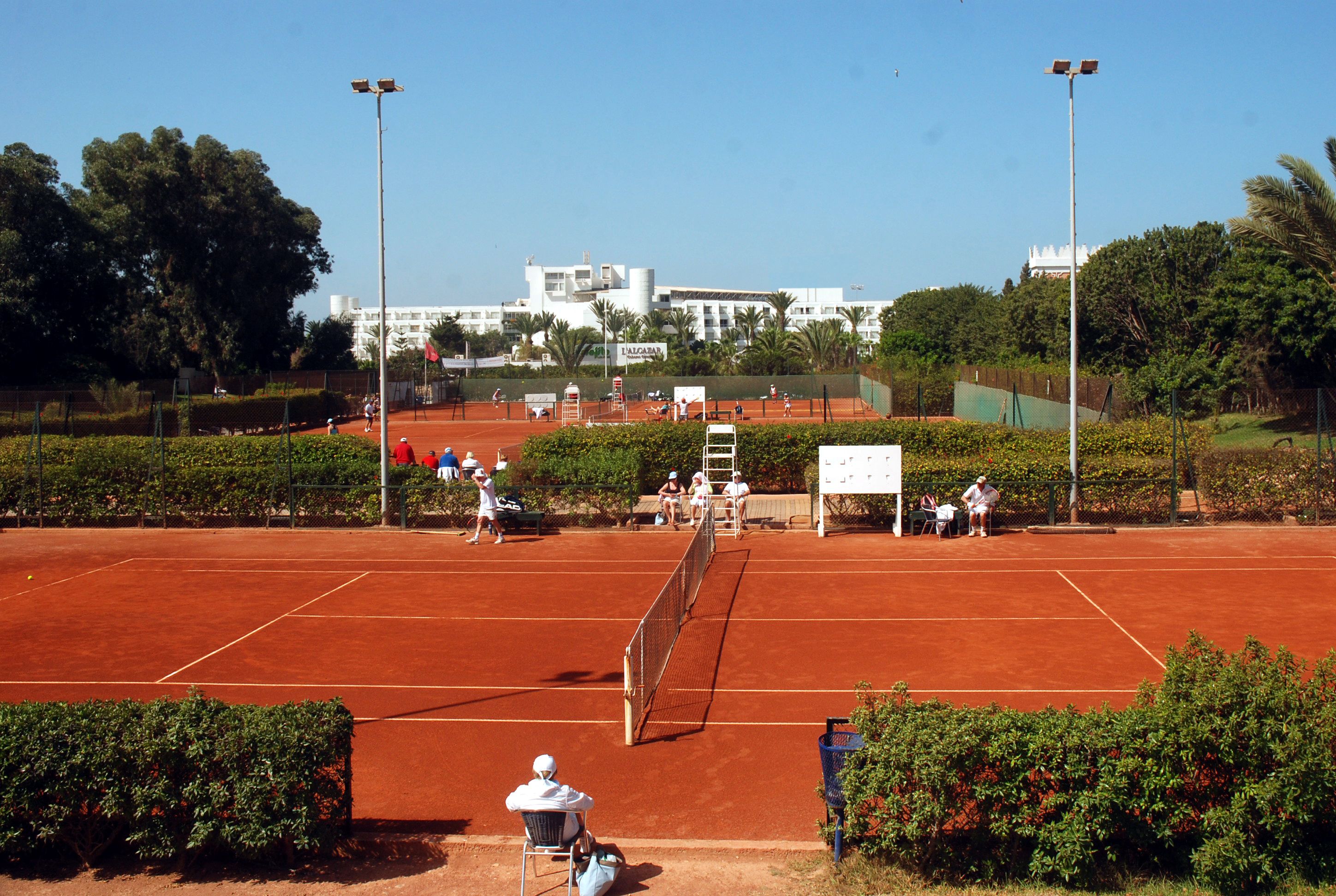 A tennis court with a net, surrounded by greenery and a building in the background.