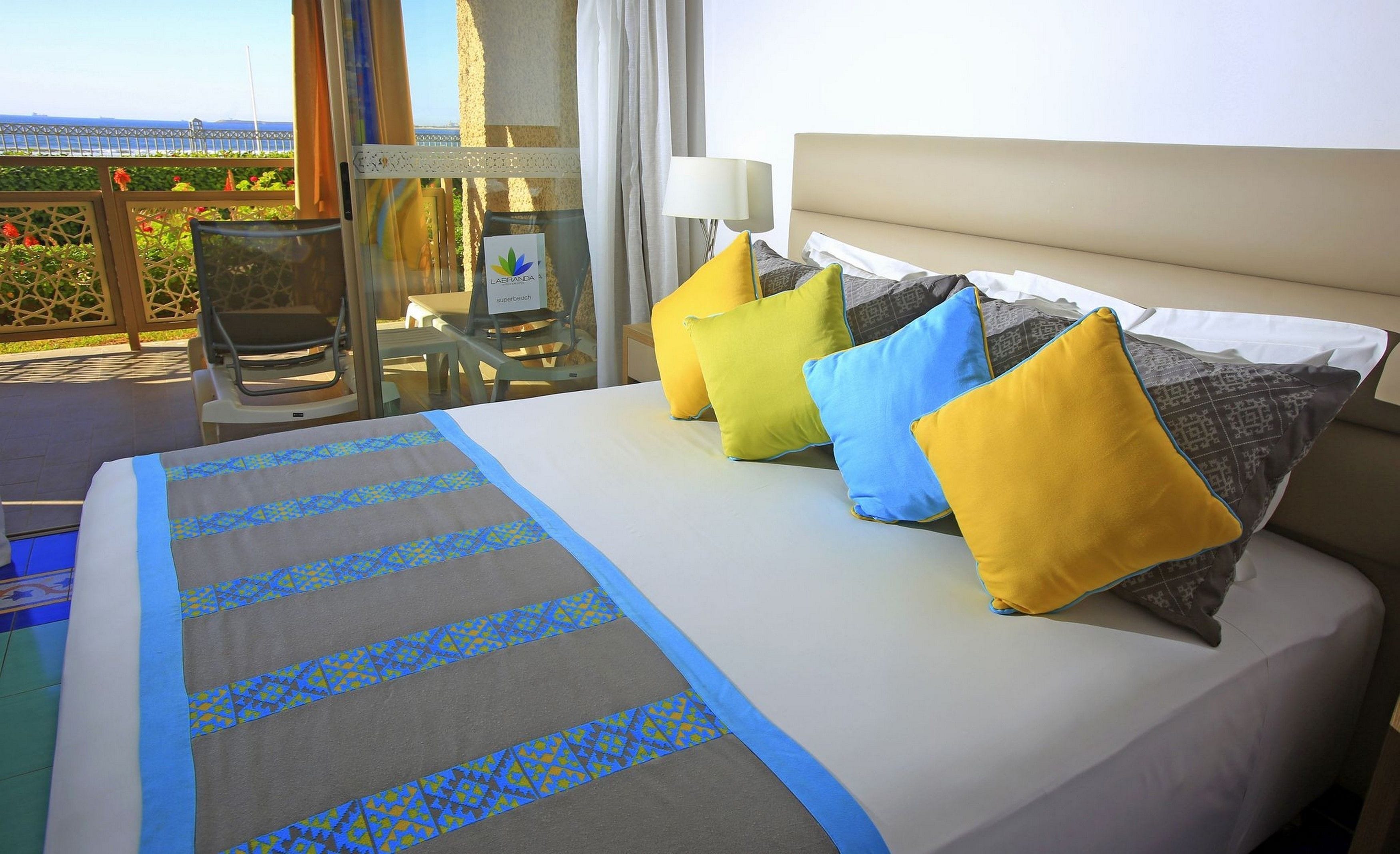 A hotel room with a bed, a view of the sea, and a balcony with outdoor furniture.