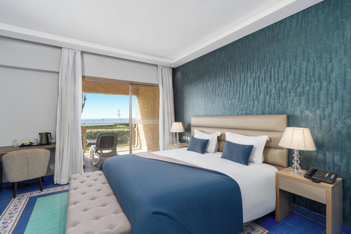 Ein Hotelzimmer mit einem großen Bett, zwei Nachttischen mit Lampen, einem Schreibtisch und einem Sessel.