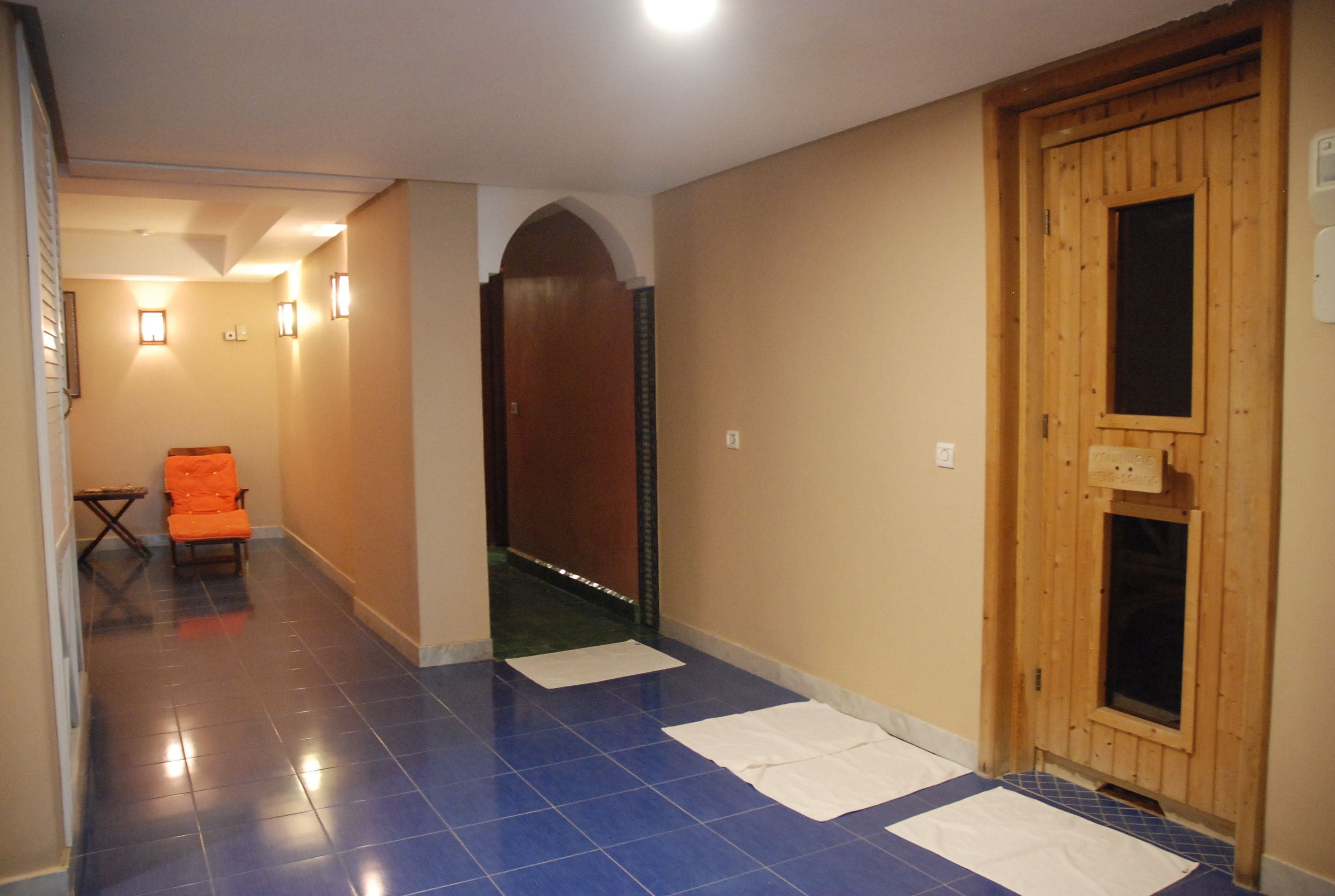 A hallway with blue-tiled flooring, a wooden door, and a small orange chair.