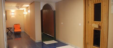 A hallway with blue-tiled flooring, a wooden door, and a small orange chair.